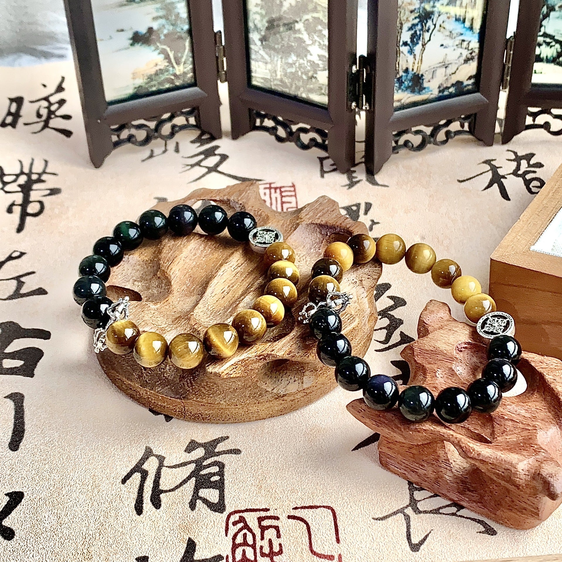 Two Tiger's Eye and Obsidian bracelets with silver charms on a wooden stand
